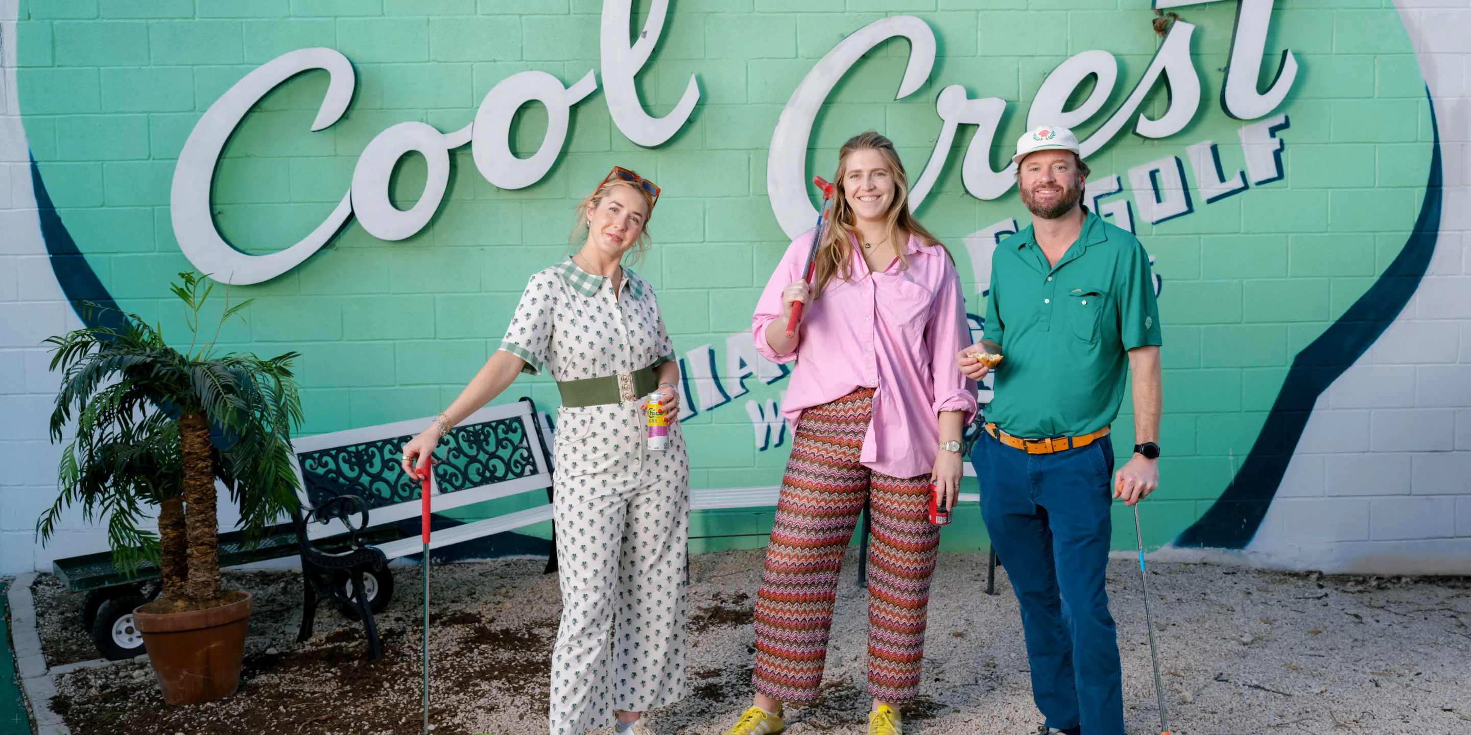 Three guests holding putters in front of the painted Cool Crest mural