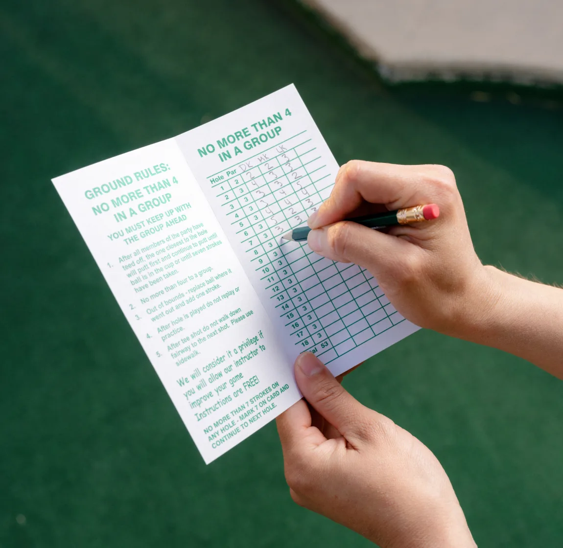 Hands filling out a Cool Crest ground-rules scorecard on the green