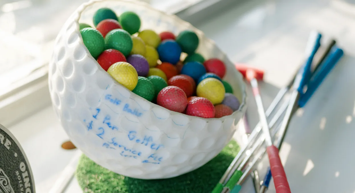 Coloured golf balls in a Cool Crest ball bucket beside putters