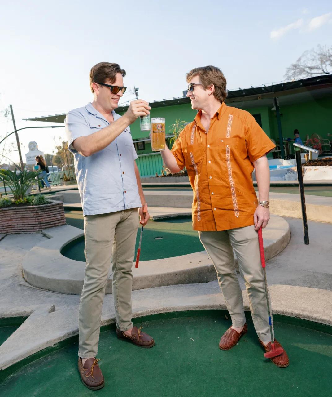 Two guests toasting drinks beside a putting green at Cool Crest